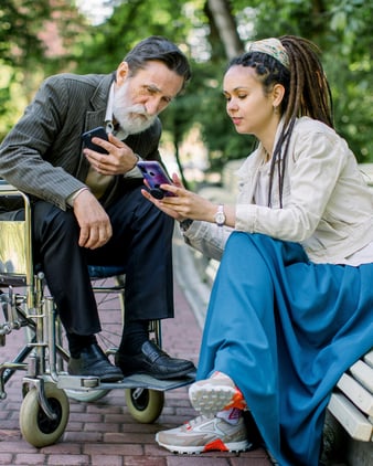 Woman sitting on a bench showing a man in a wheelchair her phone