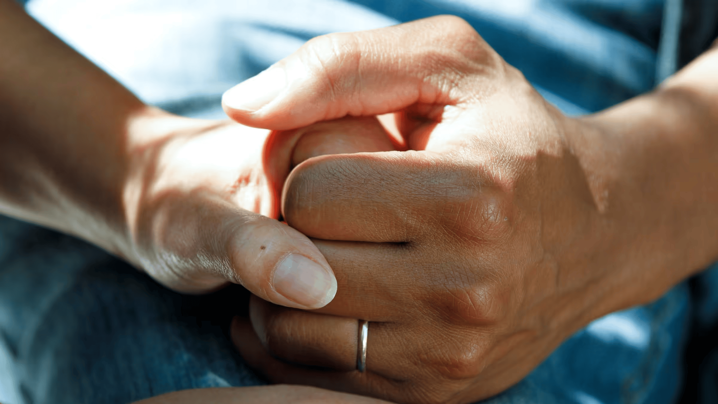 A close-up shot of two hands clasped together, one hand featuring a simple ring on the ring finger.