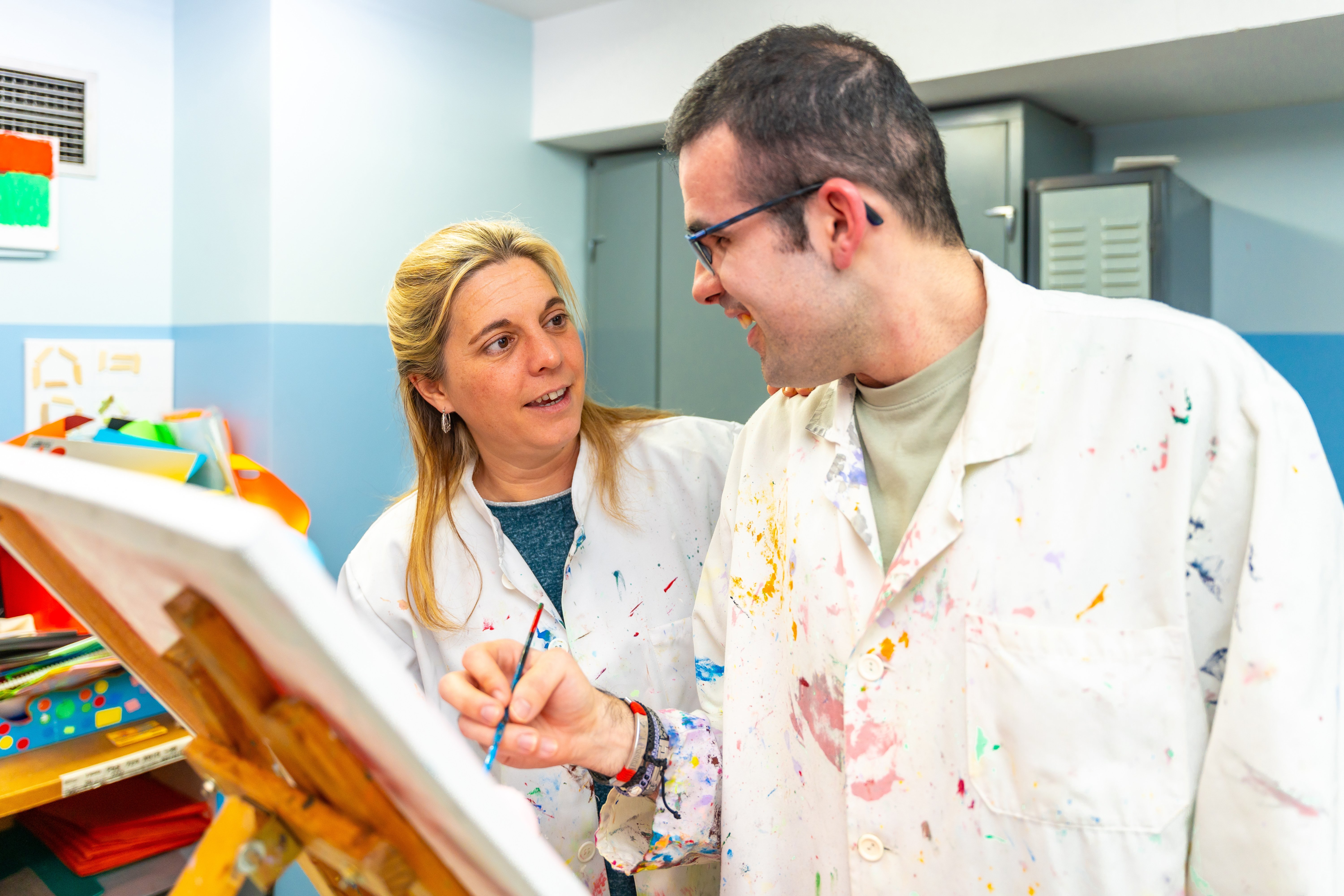 two people at a canvas looking at each other with one holding a paint brush