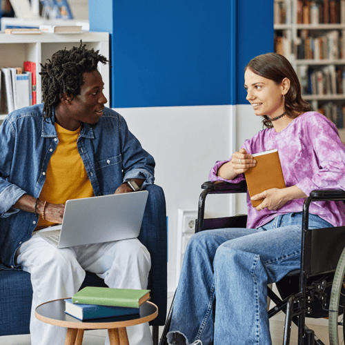 support worker and service user in library looking at laptop