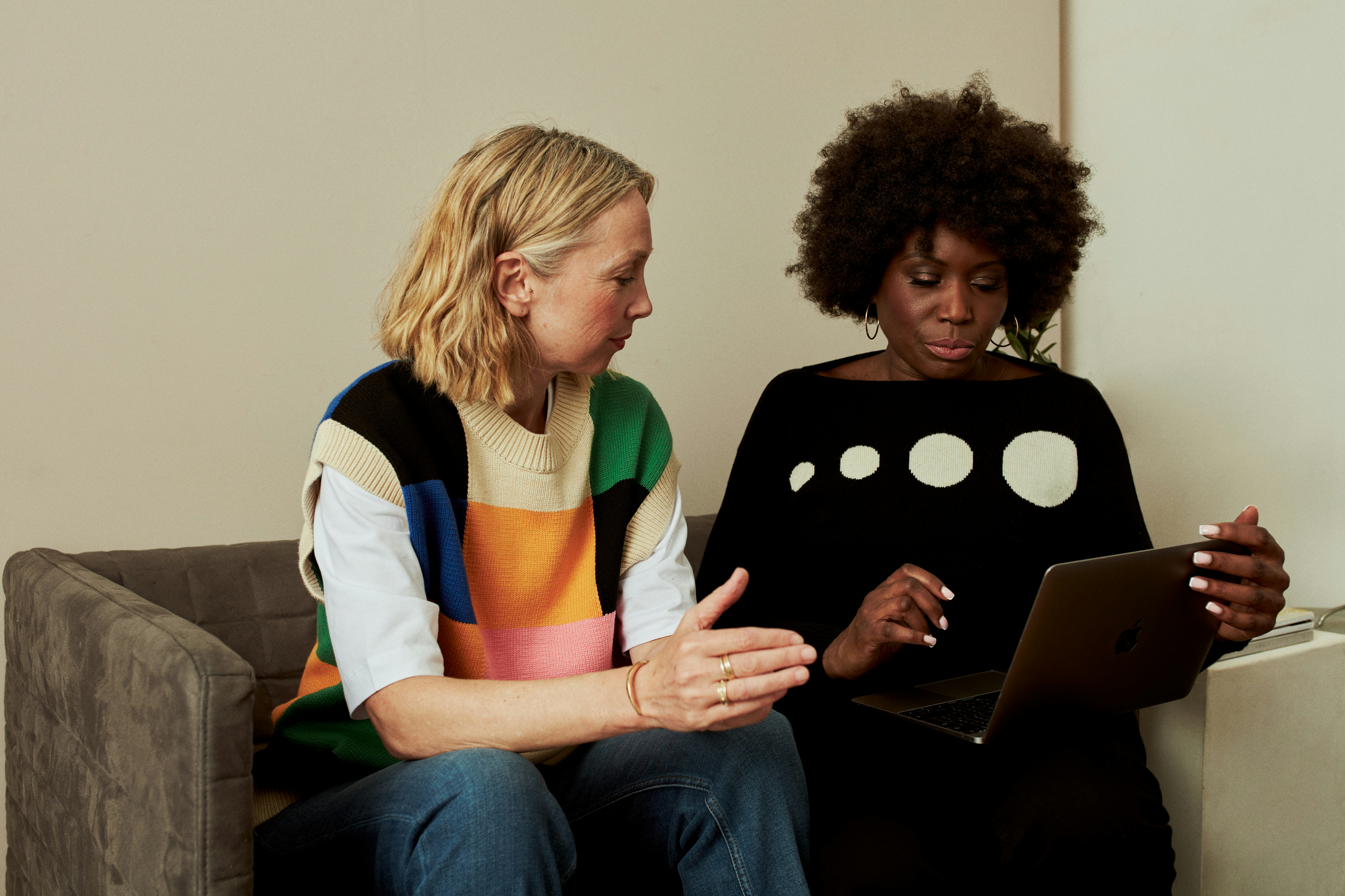 Two women on a sofa talking to each other - one is using a laptop